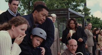 Movie still from “Stranger Than Fiction” (2006), directed by Marc Forster – A group of people gathered around a man with a helmet on his head; Medium shot, Over the shoulder angle