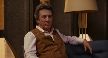 Movie still from “Stranger Than Fiction” (2006), directed by Marc Forster – A person sitting in a chair wearing a vest; Medium shot, Over the shoulder angle