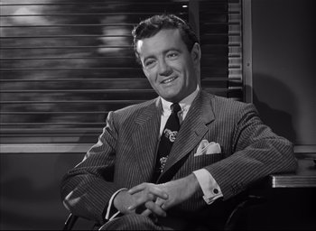 Movie still from “Strangers on a Train” (1951), directed by Alfred Hitchcock – A man sitting in a chair wearing a suit and tie; Medium shot, High angle