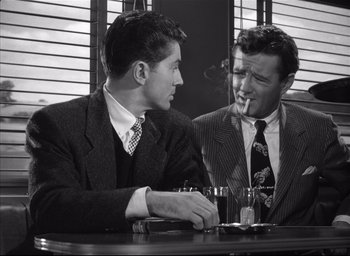 Movie still from “Strangers on a Train” (1951), directed by Alfred Hitchcock – Two men sitting at a table with a cigarette in their mouth; Medium shot, Over the shoulder angle