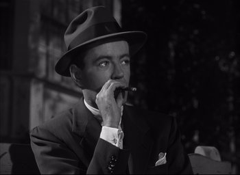 Movie still from “Strangers on a Train” (1951), directed by Alfred Hitchcock – A black and white photo of a man smoking a cigarette; Close Up shot, Low angle