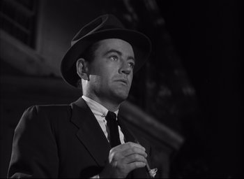 Movie still from “Strangers on a Train” (1951), directed by Alfred Hitchcock – A man wearing a suit and a hat is holding his hands together; Close Up shot, Low angle