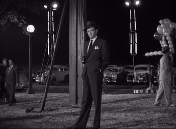Movie still from “Strangers on a Train” (1951), directed by Alfred Hitchcock – A black and white photo of a man in a suit and hat; Wide shot, Low angle