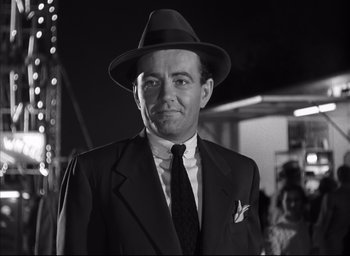 Movie still from “Strangers on a Train” (1951), directed by Alfred Hitchcock – A man in a suit and hat standing in front of a crowd of onlookers; Close Up shot, Low angle