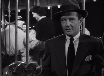 Movie still from “Strangers on a Train” (1951), directed by Alfred Hitchcock – A black and white photo of a man in a suit and hat; Medium shot, Low angle
