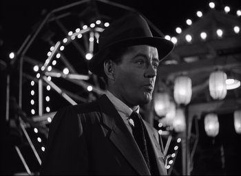 Movie still from “Strangers on a Train” (1951), directed by Alfred Hitchcock – A black and white photo of a man wearing a suit and hat; Close Up shot, Low angle