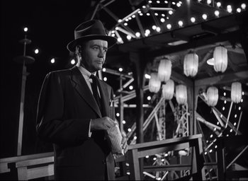 Movie still from “Strangers on a Train” (1951), directed by Alfred Hitchcock – A black and white photo of a man wearing a suit and hat; Medium shot, Low angle