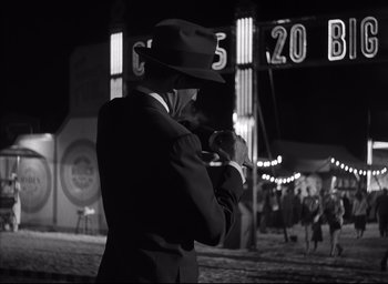 Movie still from “Strangers on a Train” (1951), directed by Alfred Hitchcock – A man in a suit and hat taking a picture; Wide shot, Over the shoulder angle