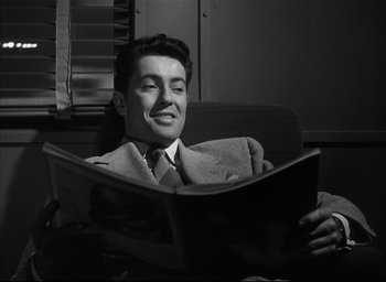 Movie still from “Strangers on a Train” (1951), directed by Alfred Hitchcock – A black and white photo of a man reading a newspaper; Medium shot, High angle