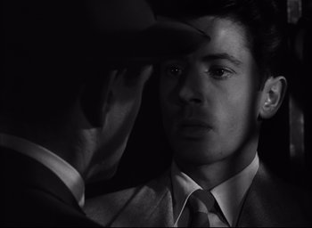 Movie still from “Strangers on a Train” (1951), directed by Alfred Hitchcock – A black and white photo of a man in a suit and tie looking into a mirror; Close Up shot, Over the shoulder angle