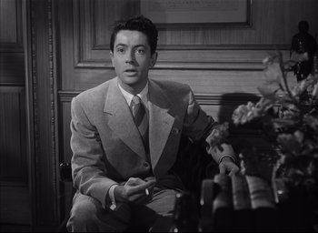 Movie still from “Strangers on a Train” (1951), directed by Alfred Hitchcock – A black and white photo of a man in a suit and tie; Medium shot, High angle