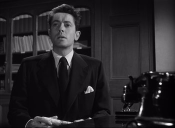 Movie still from “Strangers on a Train” (1951), directed by Alfred Hitchcock – A black and white photo of a man in a suit and tie; Medium shot, Low angle