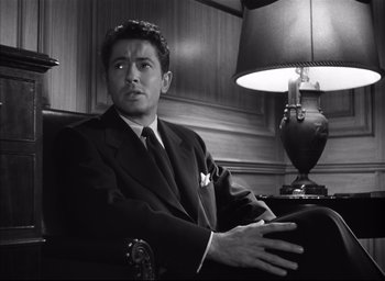 Movie still from “Strangers on a Train” (1951), directed by Alfred Hitchcock – Black and white photograph of a man in a suit and tie; Medium shot, Low angle