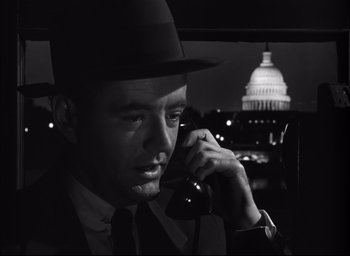 Movie still from “Strangers on a Train” (1951), directed by Alfred Hitchcock – A black and white photo of a man talking on a phone; Close Up shot, Low angle