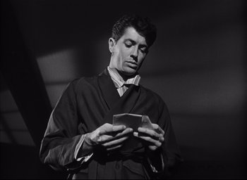Movie still from “Strangers on a Train” (1951), directed by Alfred Hitchcock – A black and white photo of a man looking down at a piece of paper; Close Up shot, Low angle