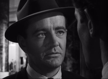 Movie still from “Strangers on a Train” (1951), directed by Alfred Hitchcock – A man wearing a suit and a hat looking to his left; Close Up shot, Over the shoulder angle