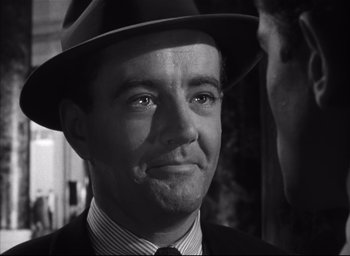 Movie still from “Strangers on a Train” (1951), directed by Alfred Hitchcock – A black and white photo of a man in a suit and a hat; Close Up shot, Over the shoulder angle