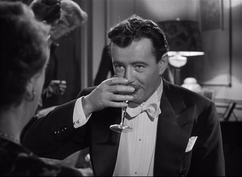 Movie still from “Strangers on a Train” (1951), directed by Alfred Hitchcock – A black and white photo of a man drinking a glass of wine; Medium shot, Over the shoulder angle