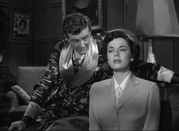 Movie still from “Strangers on a Train” (1951), directed by Alfred Hitchcock – A man and a woman sitting on a couch in a living room; Medium shot, Over the shoulder angle