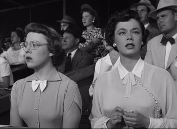 Movie still from “Strangers on a Train” (1951), directed by Alfred Hitchcock – A couple of people that are sitting in front of a crowd; Medium shot, Low angle