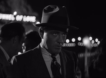 Movie still from “Strangers on a Train” (1951), directed by Alfred Hitchcock – A black and white photo of a man wearing a suit and a hat; Close Up shot, Over the shoulder angle