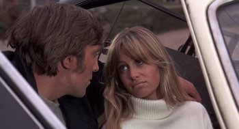 Movie still from “Straw Dogs” (1971), directed by Sam Peckinpah – A man and a woman sitting next to each other under an umbrella; Close Up shot, Low angle