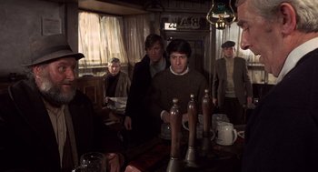 Movie still from “Straw Dogs” (1971), directed by Sam Peckinpah – A group of men standing around a table; Medium shot, Over the shoulder angle