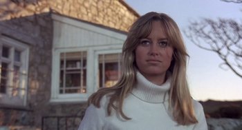 Movie still from “Straw Dogs” (1971), directed by Sam Peckinpah – A woman wearing a white sweater standing in front of a building; Close Up shot, Low angle