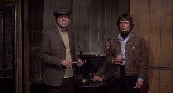 Movie still from “Straw Dogs” (1971), directed by Sam Peckinpah – A group of men standing next to each other holding drinks; Medium shot, Low angle