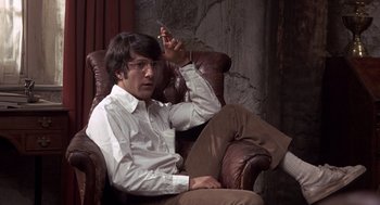 Movie still from “Straw Dogs” (1971), directed by Sam Peckinpah – A man sitting in a chair holding a cell phone; Medium shot, Low angle
