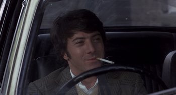 Movie still from “Straw Dogs” (1971), directed by Sam Peckinpah – A man sitting in the drivers seat of a car while smoking a cigarette; Close Up shot, Over the shoulder angle