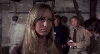 Movie still from “Straw Dogs” (1971), directed by Sam Peckinpah – A young woman is standing in front of two other people; Close Up shot, Over the shoulder angle