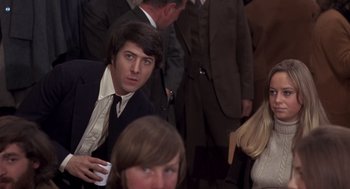 Movie still from “Straw Dogs” (1971), directed by Sam Peckinpah – A man in a suit and tie holding a cup; Medium shot, Over the shoulder angle