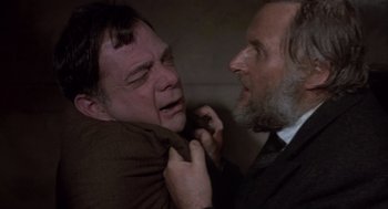 Movie still from “Straw Dogs” (1971), directed by Sam Peckinpah – Two men in business suits and ties one of which is holding a knife to the other's neck; Close Up shot, Over the shoulder angle