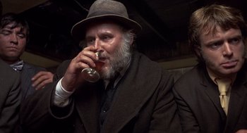 Movie still from “Straw Dogs” (1971), directed by Sam Peckinpah – An old man with a beard drinking a glass of wine; Close Up shot, Over the shoulder angle