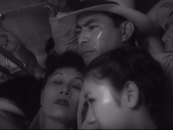 Movie still from “Stray Dog” (1949), directed by Akira Kurosawa – A group of people sitting next to each other in a room; Close Up shot, High angle