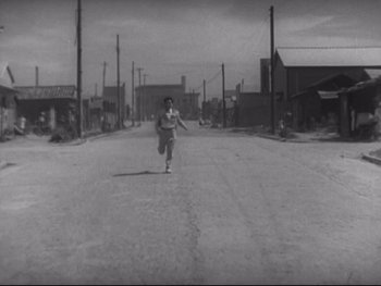 Movie still from “Stray Dog” (1949), directed by Akira Kurosawa – A man running down the middle of a street; Extreme Wide shot, High angle