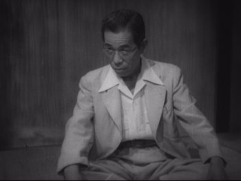 Movie still from “Stray Dog” (1949), directed by Akira Kurosawa – An older man sitting on the ground wearing a suit; Medium shot, High angle