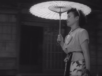 Movie still from “Stray Dog” (1949), directed by Akira Kurosawa – A woman holding an open umbrella while standing outside; Medium shot, Low angle