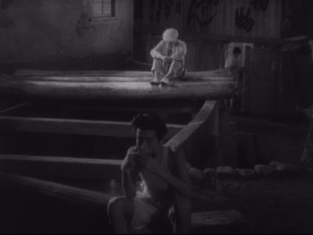 Movie still from “Stray Dog” (1949), directed by Akira Kurosawa – A man sitting on a bench next to a woman eating; Wide shot, High angle