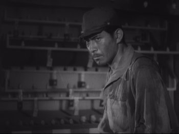 Movie still from “Stray Dog” (1949), directed by Akira Kurosawa – A black and white photo of a man wearing a hat and overalls; Close Up shot, High angle