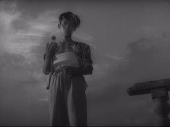 Movie still from “Stray Dog” (1949), directed by Akira Kurosawa – A black and white photo of a woman holding a flower; Medium shot, Low angle