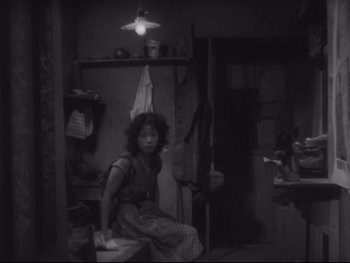 Movie still from “Stray Dog” (1949), directed by Akira Kurosawa – A black and white photo of a woman sitting in a room; Medium shot, High angle