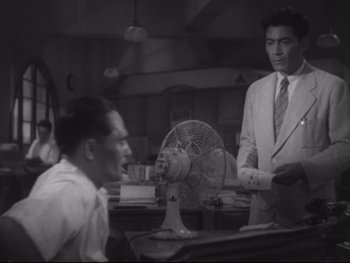 Movie still from “Stray Dog” (1949), directed by Akira Kurosawa – Two men in suits and ties are standing in front of an electric fan; Medium shot, High angle