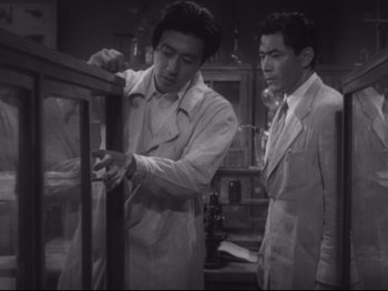 Movie still from “Stray Dog” (1949), directed by Akira Kurosawa – Two men in white jackets looking at a display case; Medium shot, High angle
