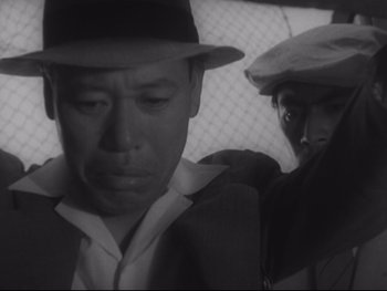 Movie still from “Stray Dog” (1949), directed by Akira Kurosawa – A man wearing a hat standing next to another man wearing a hat; Close Up shot, Low angle
