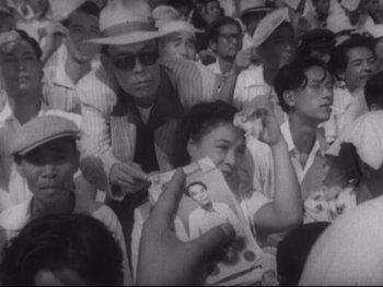 Movie still from “Stray Dog” (1949), directed by Akira Kurosawa – A crowd of people sitting and standing in a room; Medium shot, High angle