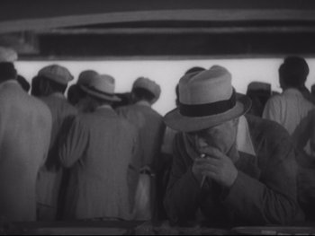 Movie still from “Stray Dog” (1949), directed by Akira Kurosawa – An older man smoking a cigarette in front of a group of people; Medium shot, High angle