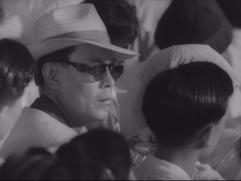 Movie still from “Stray Dog” (1949), directed by Akira Kurosawa – An older man wearing a white hat and sunglasses; Close Up shot, Low angle