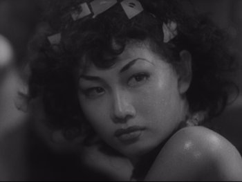 Movie still from “Stray Dog” (1949), directed by Akira Kurosawa – A black and white photo of a woman with her head tilted to the side; Close Up shot, High angle